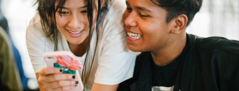 two friends smiling and looking at a mobile device