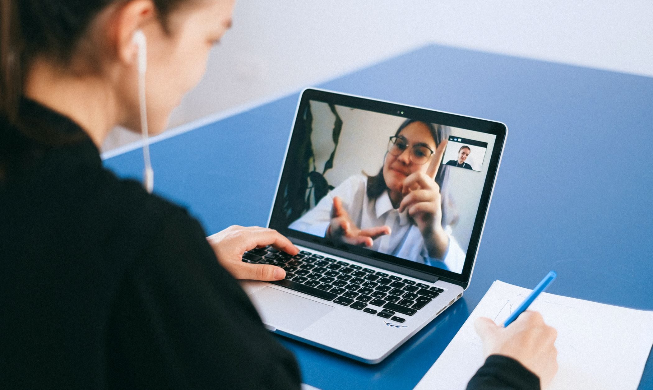 A woman sitting out of focus having a conversation with another woman via video chat on her laptop.